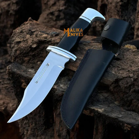 A Clip-Point Bowie Knife with a D2 steel blade and G10 handle, accompanied by a leather sheath, displayed on a rugged outdoor background.