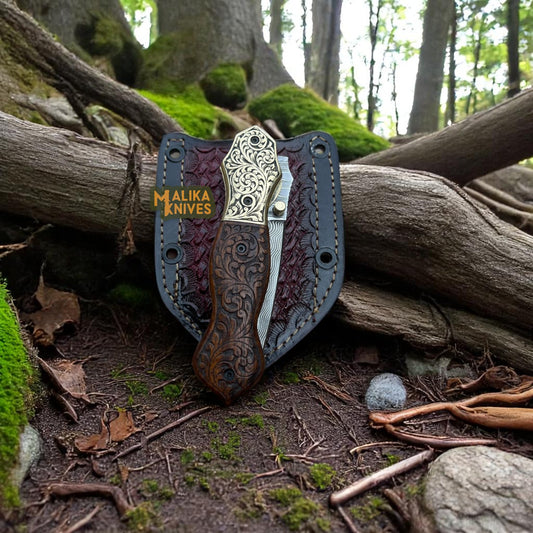 Close-up of hand-engraved folding knife in closed position, angled at 90 degrees, resting on its custom sheath.