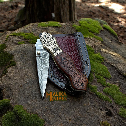 Partially open Damascus steel folding knife forming a V-shape, blade facing downward, resting on leather sheath.