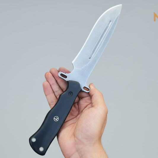 Hand holding a knife with 'Malika Knives' branding on a wooden surface