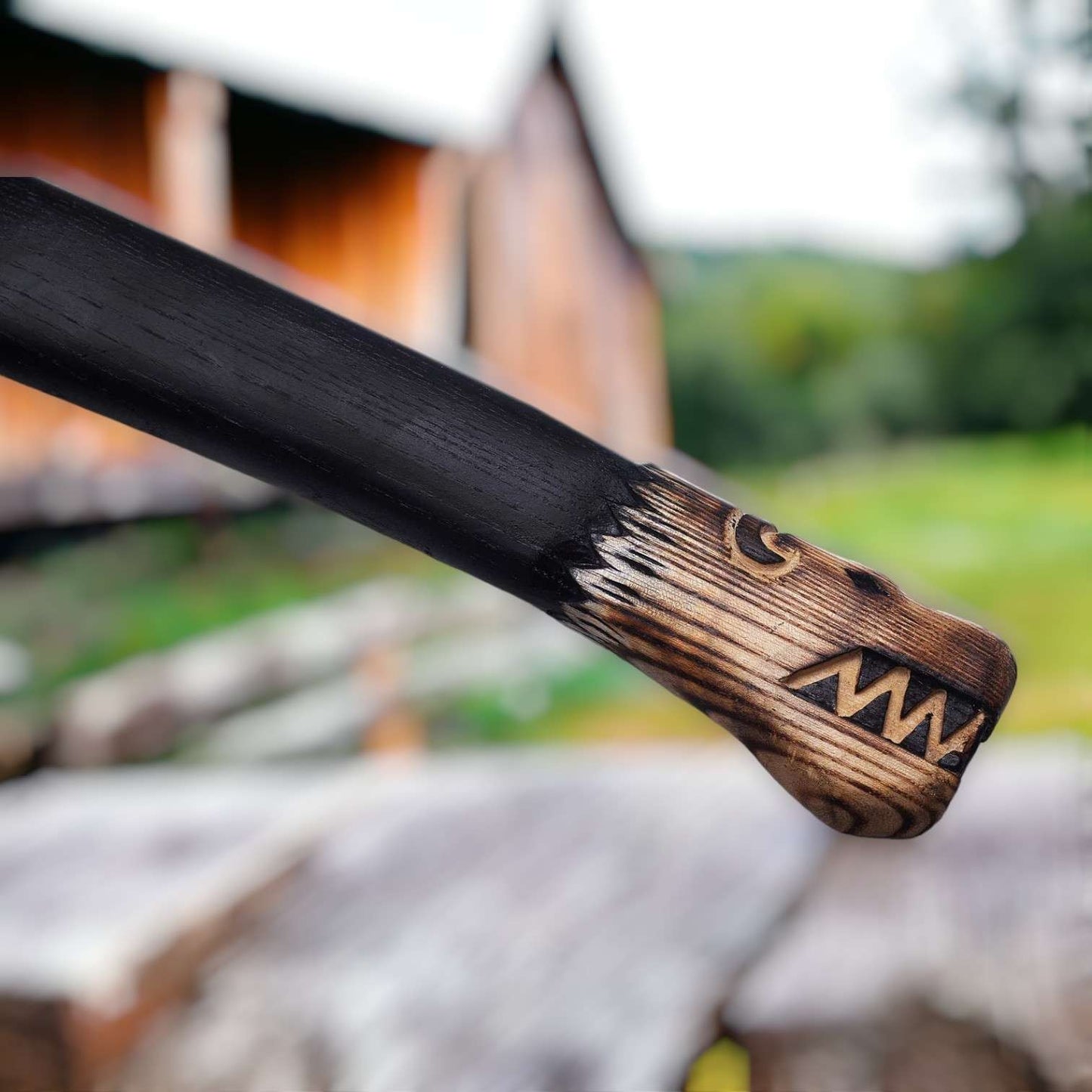 Hand-forged Norse bearded axe with wolf-engraved head and carved ash scale-grip handle against a barn