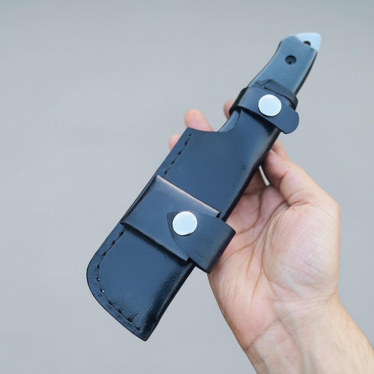 Hand holding a black leather knife sheath against a gray background
