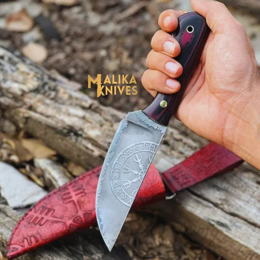 A hand holding a Viking hunting knife with a Micarta handle and a hand engraved cowhide leather sheath in the background.