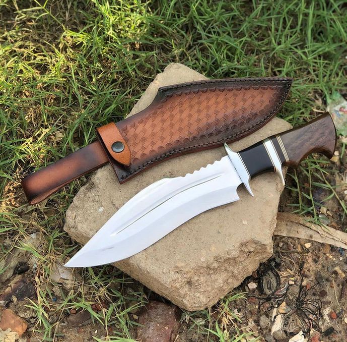 D2 Bowie Knife with a brown leather sheath on a rock in a natural setting