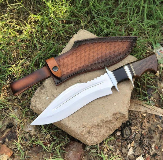 D2 Bowie Knife with a brown leather sheath on a rock in a natural setting