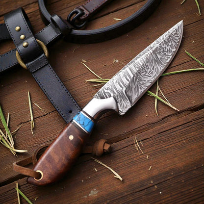 Damascus cowboy hunting knife with rosewood handle and turquoise spacer resting on a basket-tooled pancake leather sheath on a wooden ranch table.