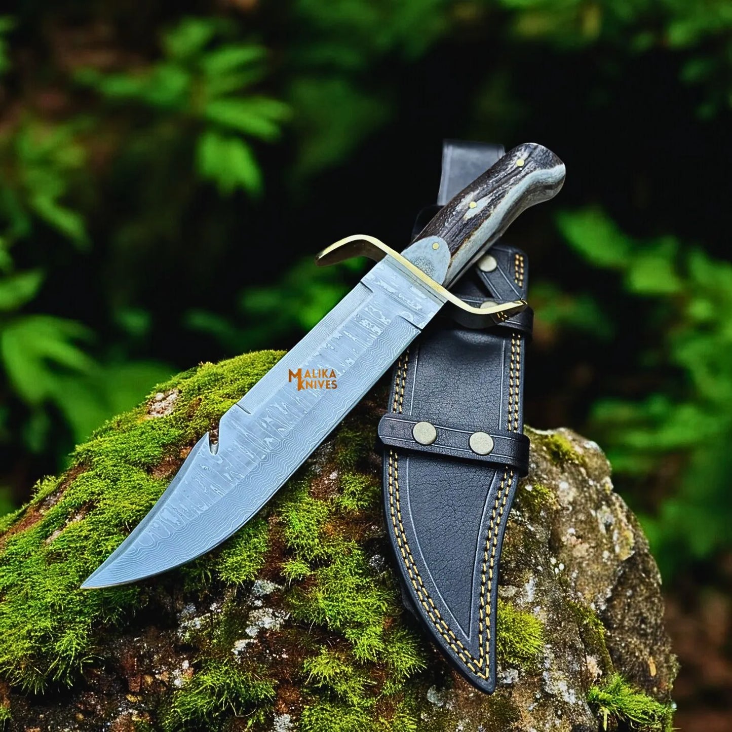SS Damascus Gut Hook Bowie Knife with leather sheath on a mossy rock with a blurred green background
