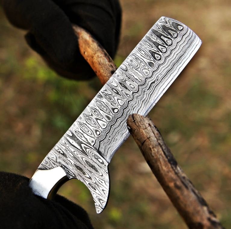 Damascus steel Bull Cutter knife held by hand cuuting the wooden branch against a blurred natural background