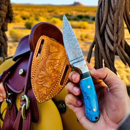 Hand holding a blue-handled Cowboy Hunting knife with a desert landscape in the background