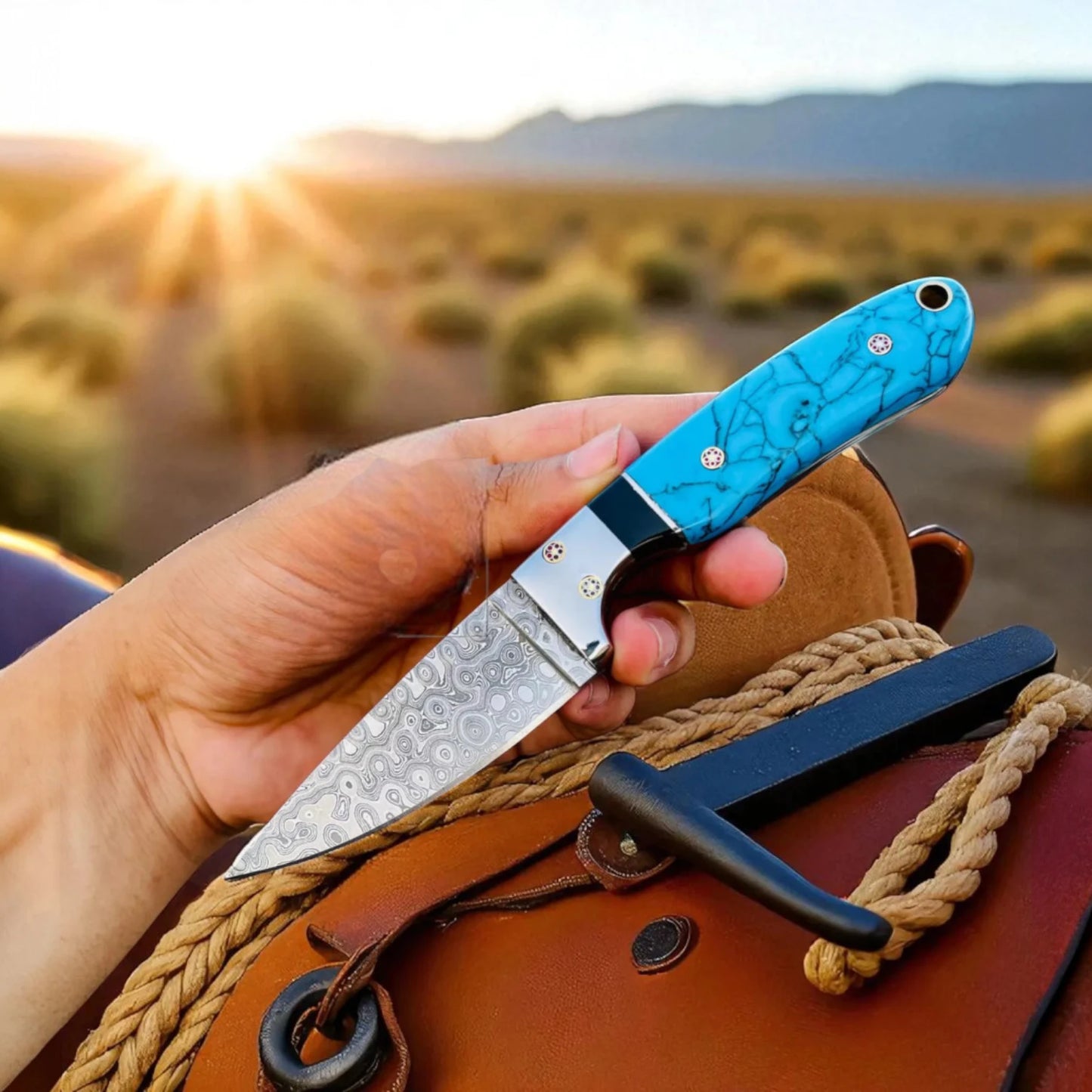 Hand holding a Cowboy hunting knife with a blue Marble handle against a desert landscape