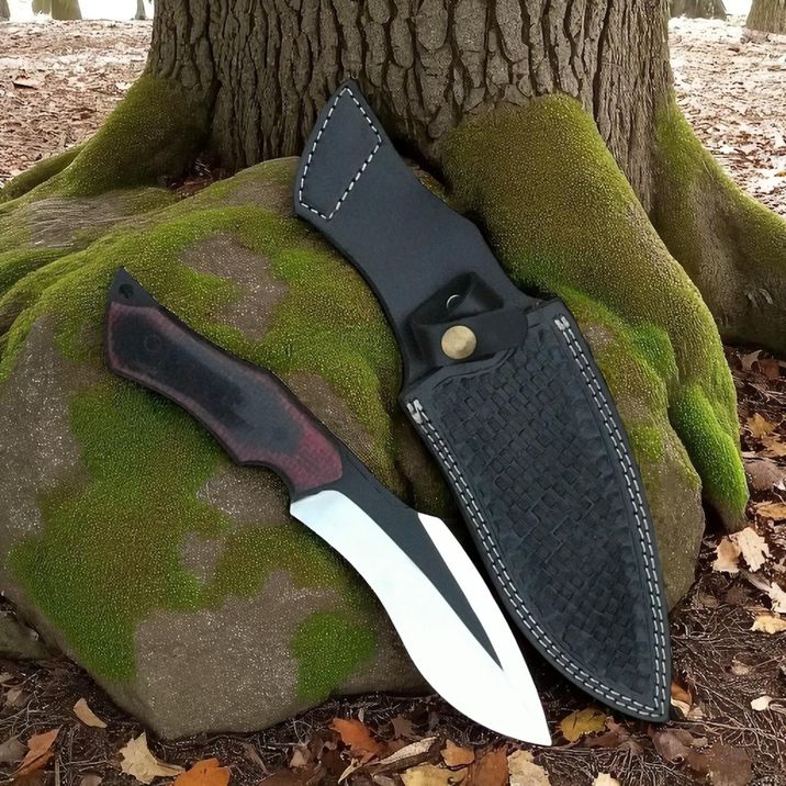 Bowie Knife with a black sheath leaning against a tree trunk in a forest setting