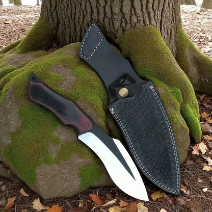 Bowie Knife with a black sheath leaning against a tree trunk in a forest setting