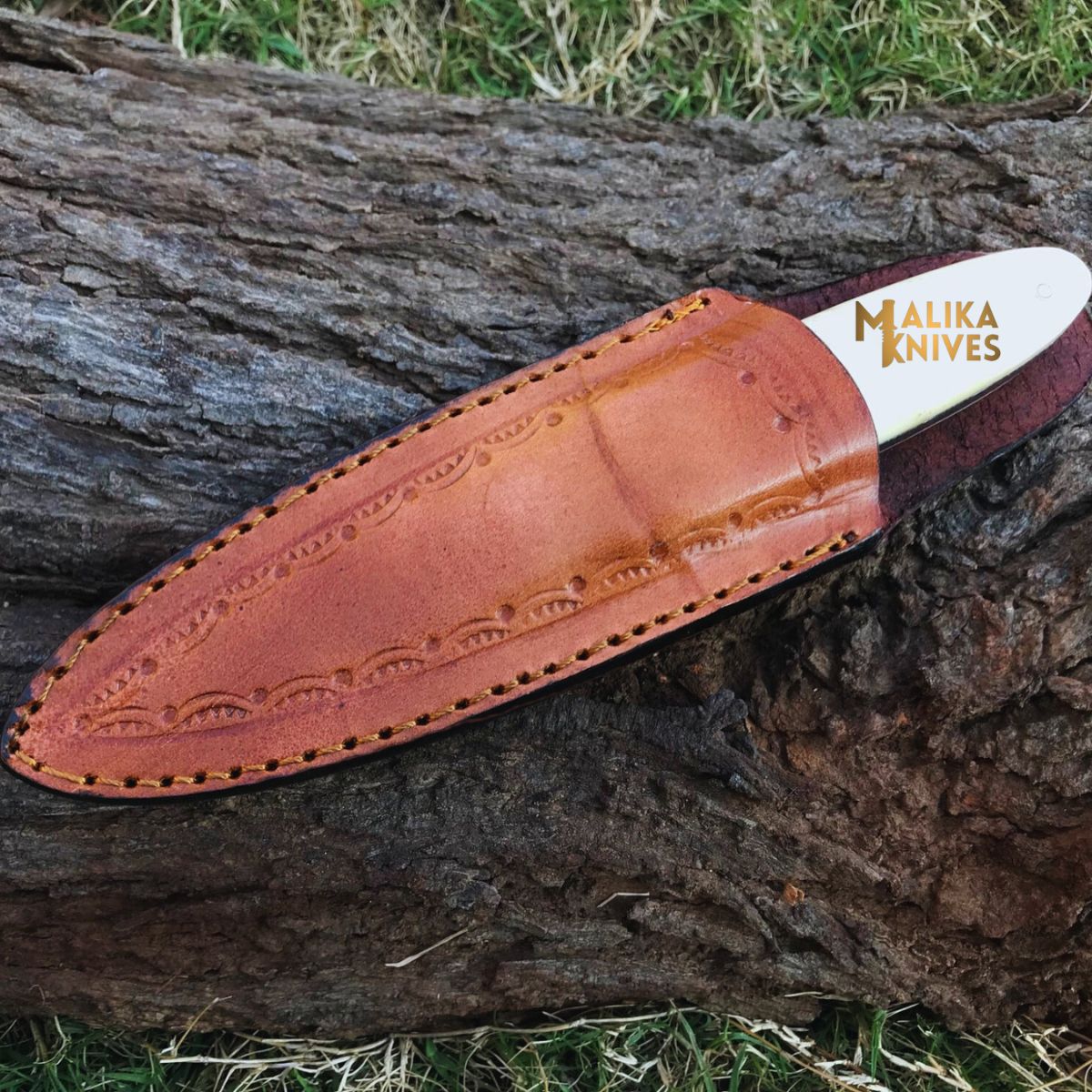 handmade d2 needle point hunting knife with camel bone handle in leather sheath on wooden surface