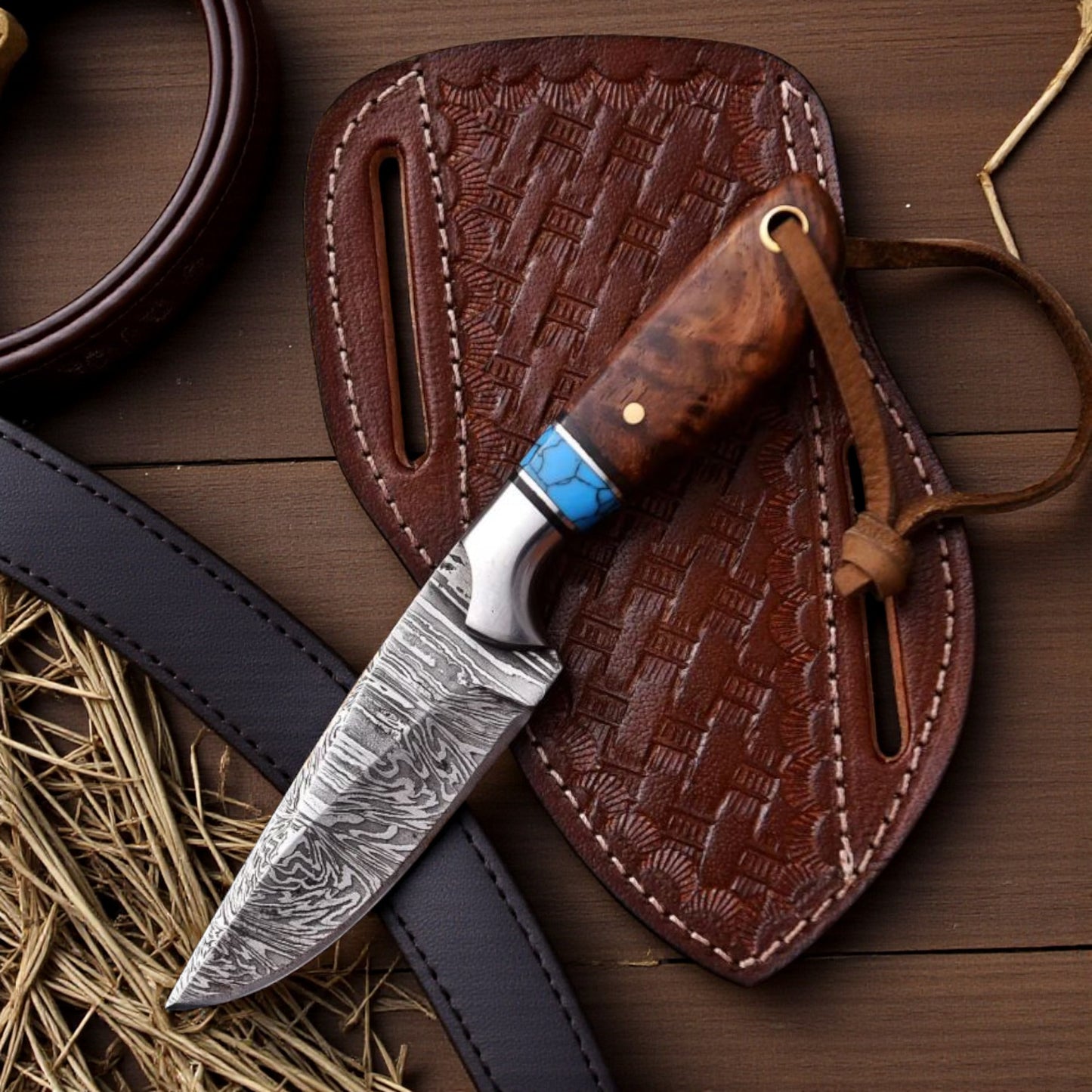 Damascus cowboy hunting knife with rosewood handle and turquoise spacer resting on a basket-tooled pancake leather sheath on a wooden ranch table.