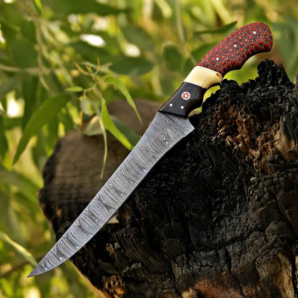 Handmade Damascus fish fillet knife with flexible blade and red honeycomb camel bone handle on a wood stump