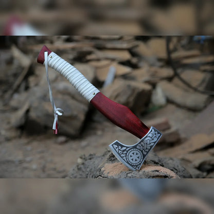 Viking bearded hatchet with Norse sunwheel engraved head and leather-wrapped red handle standing on stone