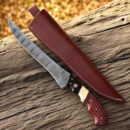 Damascus fish fillet knife with red honeycomb handle beside a brown leather sheath on driftwood