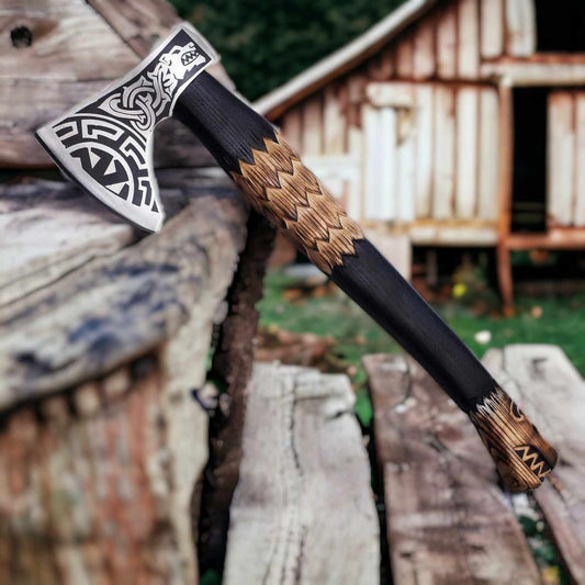 Hand-forged Norse bearded axe with wolf-engraved head and carved ash scale-grip handle against a barn