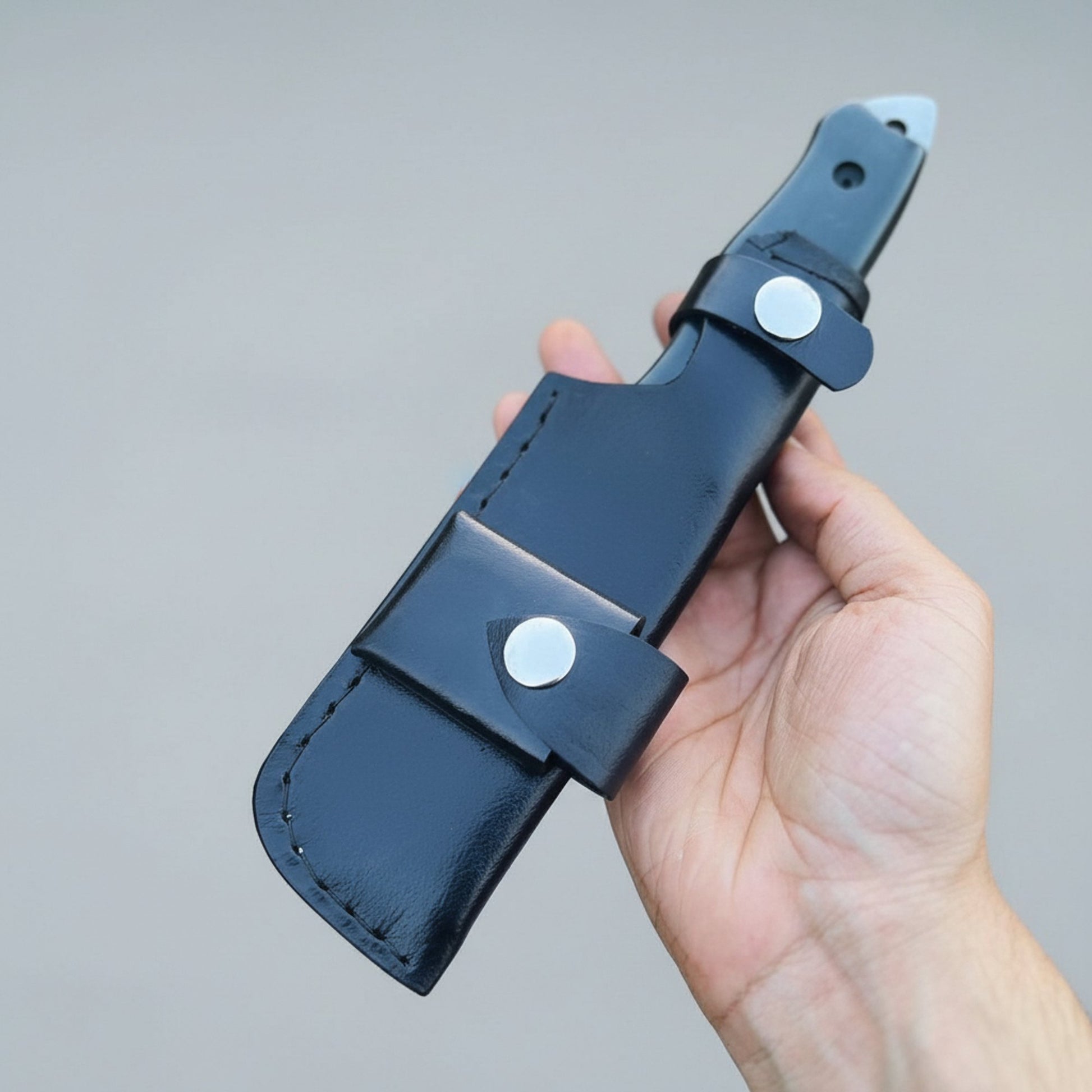 Hand holding a black leather knife sheath against a gray background