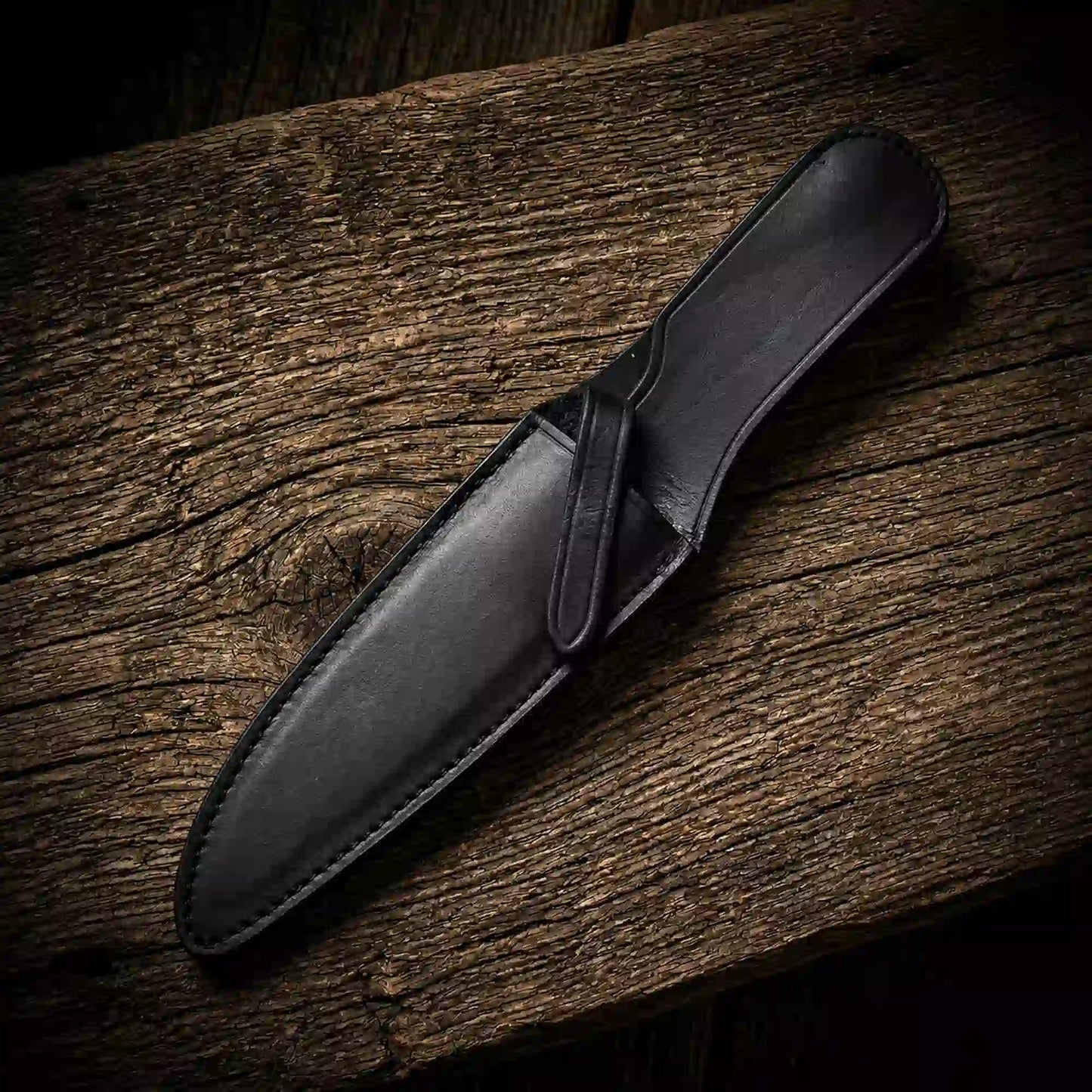 Black leather sheath for a Rambo-style survival bowie knife on weathered wood