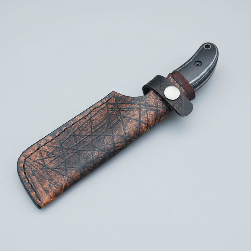 Knife with leather sheath held by a hand on a wooden surface, branded 'Malika Knives'.