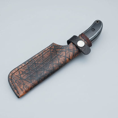 Knife with leather sheath held by a hand on a wooden surface, branded 'Malika Knives'.