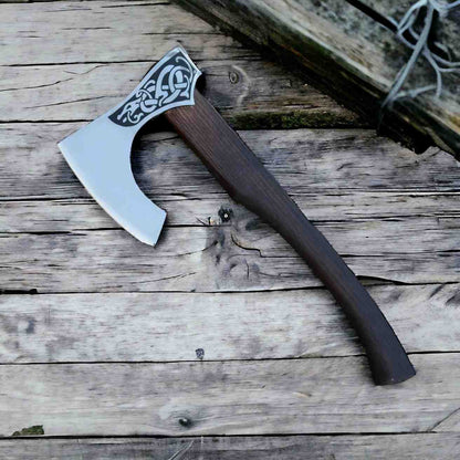 Viking bearded axe with Norse serpent engraved head and rosewood handle standing on a stump