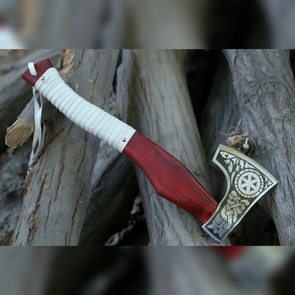 Norse Viking axe with Kolovrat sunwheel and rune engraved head and red wood handle on logs