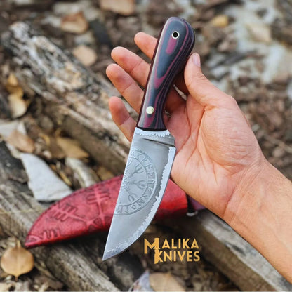 A hand holding a Viking hunting knife with a Micarta handle and a hand-engraved cowhide leather sheath in the background.